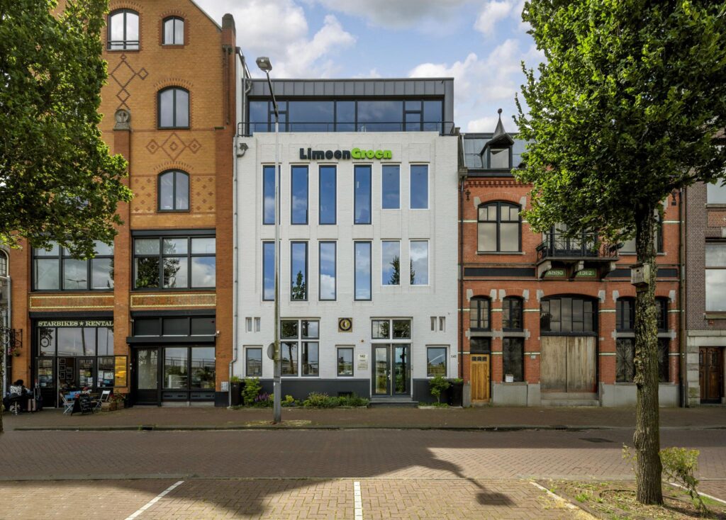 Voorgevel van moderne en historische panden aan de De Ruijterkade in Amsterdam, met in het midden het witte kantoorgebouw van LimoenGroen.